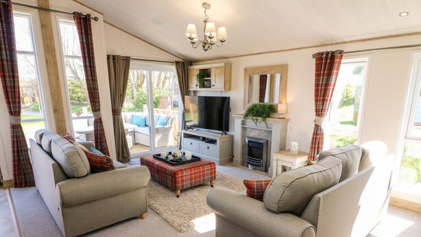A cozy living room with two sofas, a coffee table, a fireplace, and a TV. - Curlew Lodge (Carnforth)
