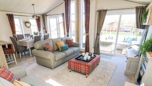A cozy living room with a sofa, a coffee table, and a dining area with chairs and a table. - Curlew Lodge (Carnforth)