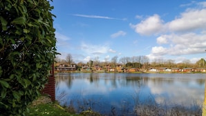 A lakeside view with wooden cabins and a grassy area. - Curlew Lodge (Carnforth)