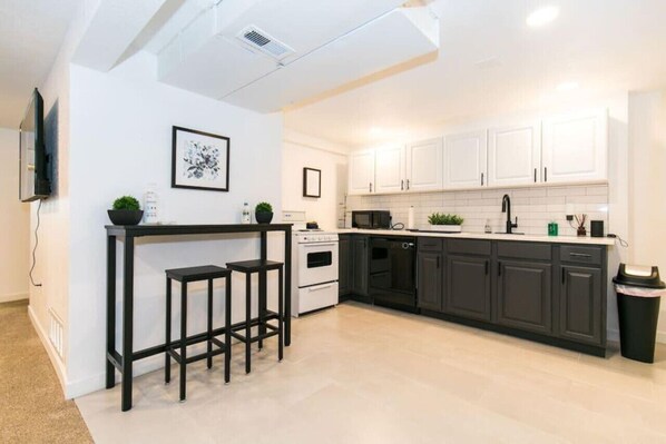 Enjoy quick refreshments at the sleek bar counter with stools, complemented by white cabinetry and a range hood.