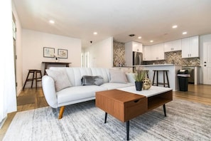 Relax in this stylish living space with a sofa, coffee table, and kitchen featuring a herringbone-patterned backsplash and stainless steel appliances.