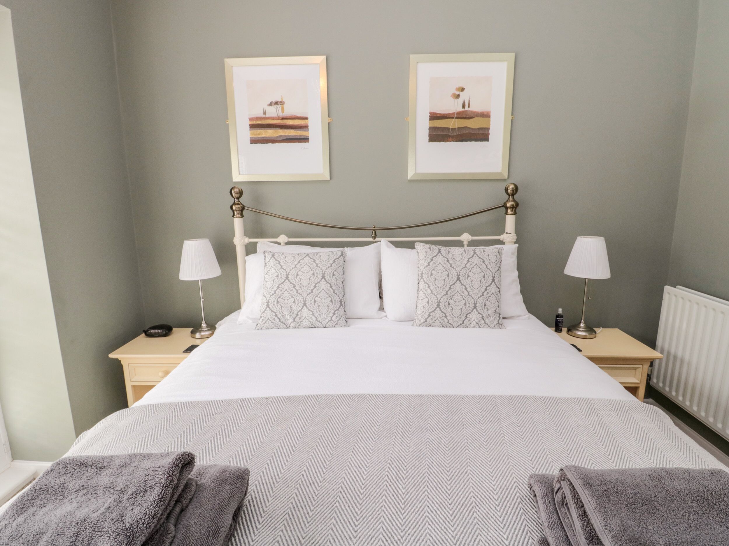 A neatly made bed with white linens and patterned pillows, two bedside tables with lamps, and two framed pictures on the wall.