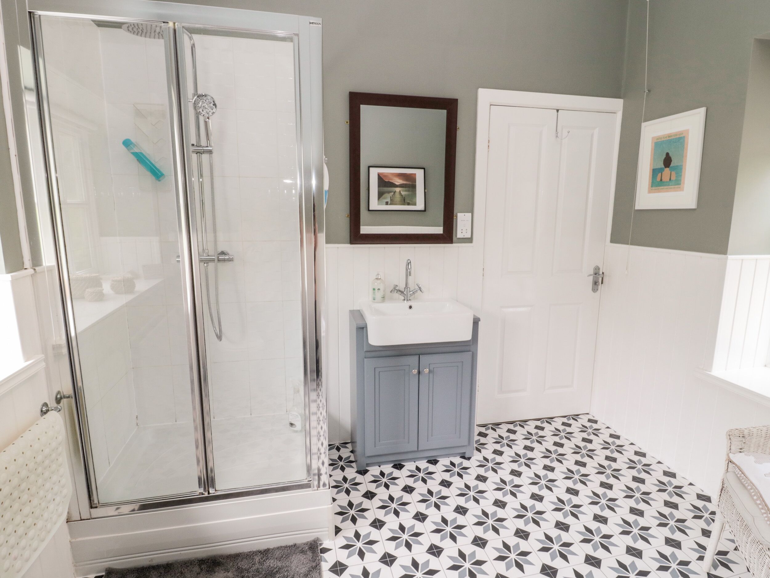 A bathroom with a glass-enclosed shower, a sink with a mirror above it, and a patterned floor.