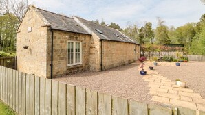 Une petite maison en pierre avec un toit en pente, une fenêtre et une allée gravillonnée.