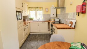 Une cuisine compacte avec une table en bois, des placards, une cuisinière et une couverture anti-feu accrochée au mur.