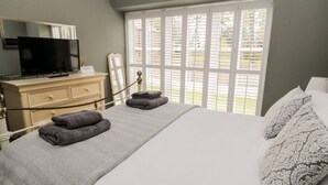 Une chambre à coucher comprenant un lit, une commode, un téléviseur et une fenêtre avec des stores.