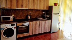 A compact kitchen with wooden cabinets, a microwave, a washing machine, and a refrigerator. - Lovely apartment for rent in a quiet Sofia suburb. (Sofia)