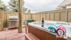 Boblebad med håndklæder og en flaske vin, grill og en træterrasse.