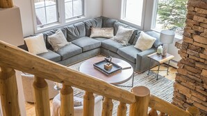 En moderne stue med en grå hjørnesofa, et rundt sofabord og en trappe i træ.