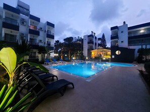 Una piscina con lettini, circondata da edifici moderni con balconi e condizionatori.