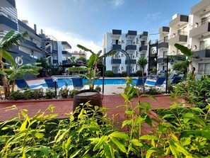 Area piscina con sedie a sdraio, cielo sereno e moderni edifici sullo sfondo.