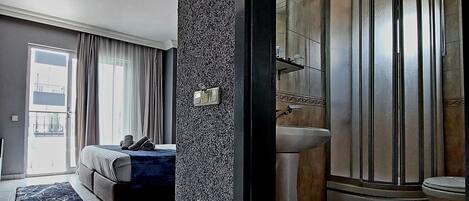 A modern hotel room with a bed, a bathroom with a shower, and a view of the outside.