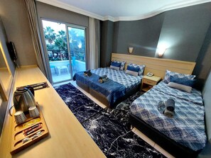 Una camera d'hotel con due letti, un piccolo tavolo con bollitore e tazze, un comodino con un telefono, e vista su una piscina e palme attraverso la porta in vetro.