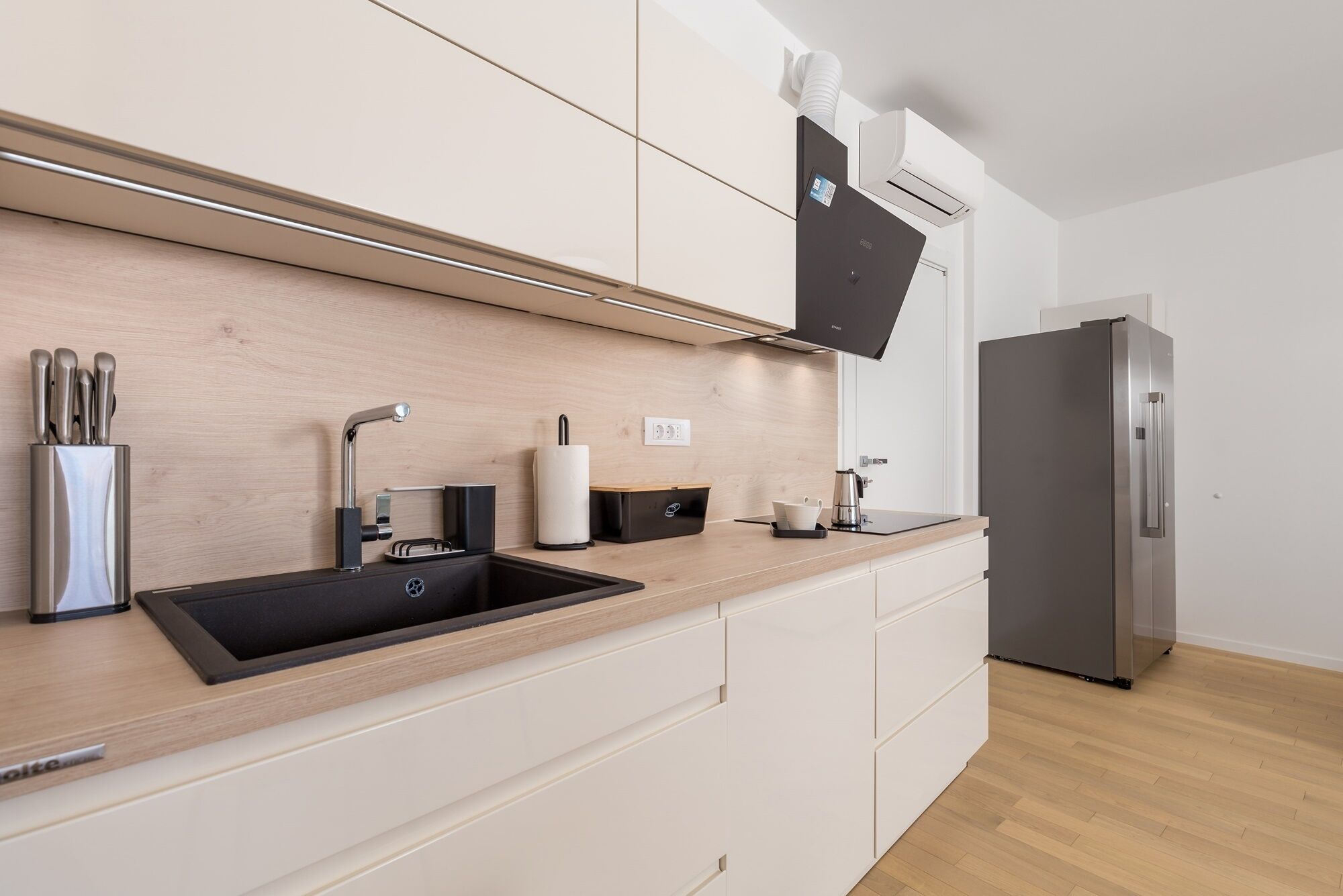 Een moderne keuken met een zwarte spoelbak, roestvrijstalen apparatuur en een houten aanrecht.