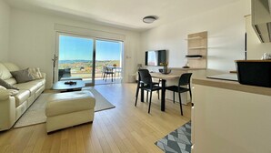 A modern living room with a sofa, a coffee table, and a dining area with chairs and a TV. - Premium Apartment Panoramico – Spacious 4-Star Holiday Apartment with a Sea view (Krk)
