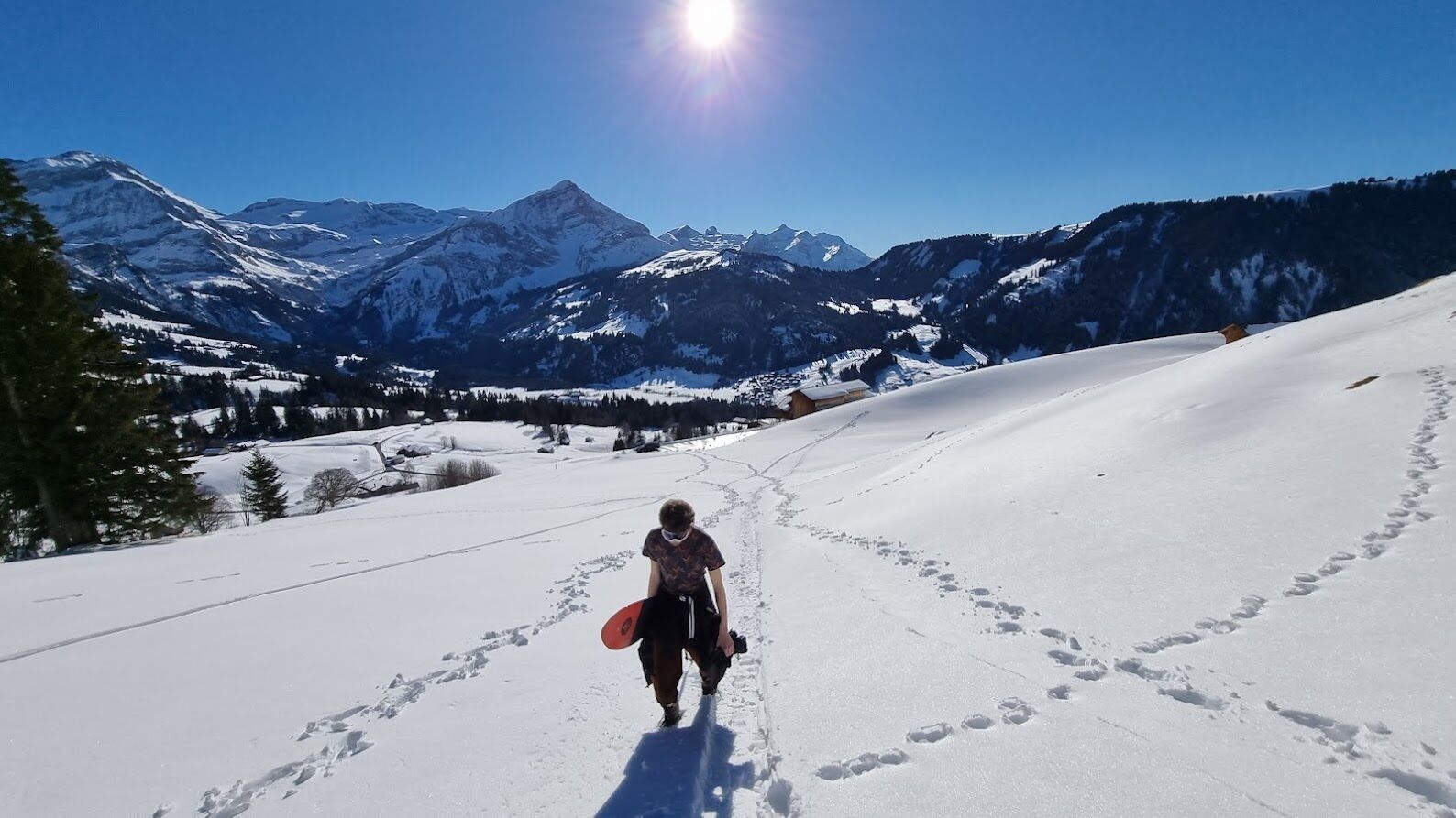 A snowy mountain path with footprints and a person carrying a snowboard.