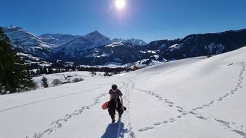 A snowy mountain path with footprints and a person carrying a snowboard.