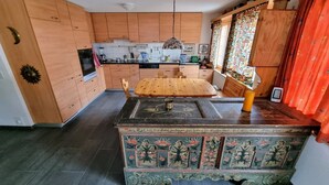 A kitchen with wooden cabinets, a dining table, and a decorative chest. - Room with extra-large double-bed, cable TV, private bathroom, organic breakfast, (Lauenen)
