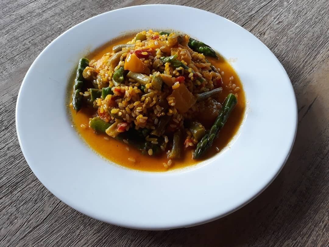 A white plate with a dish of rice and vegetables, possibly a curry, on a wooden table.