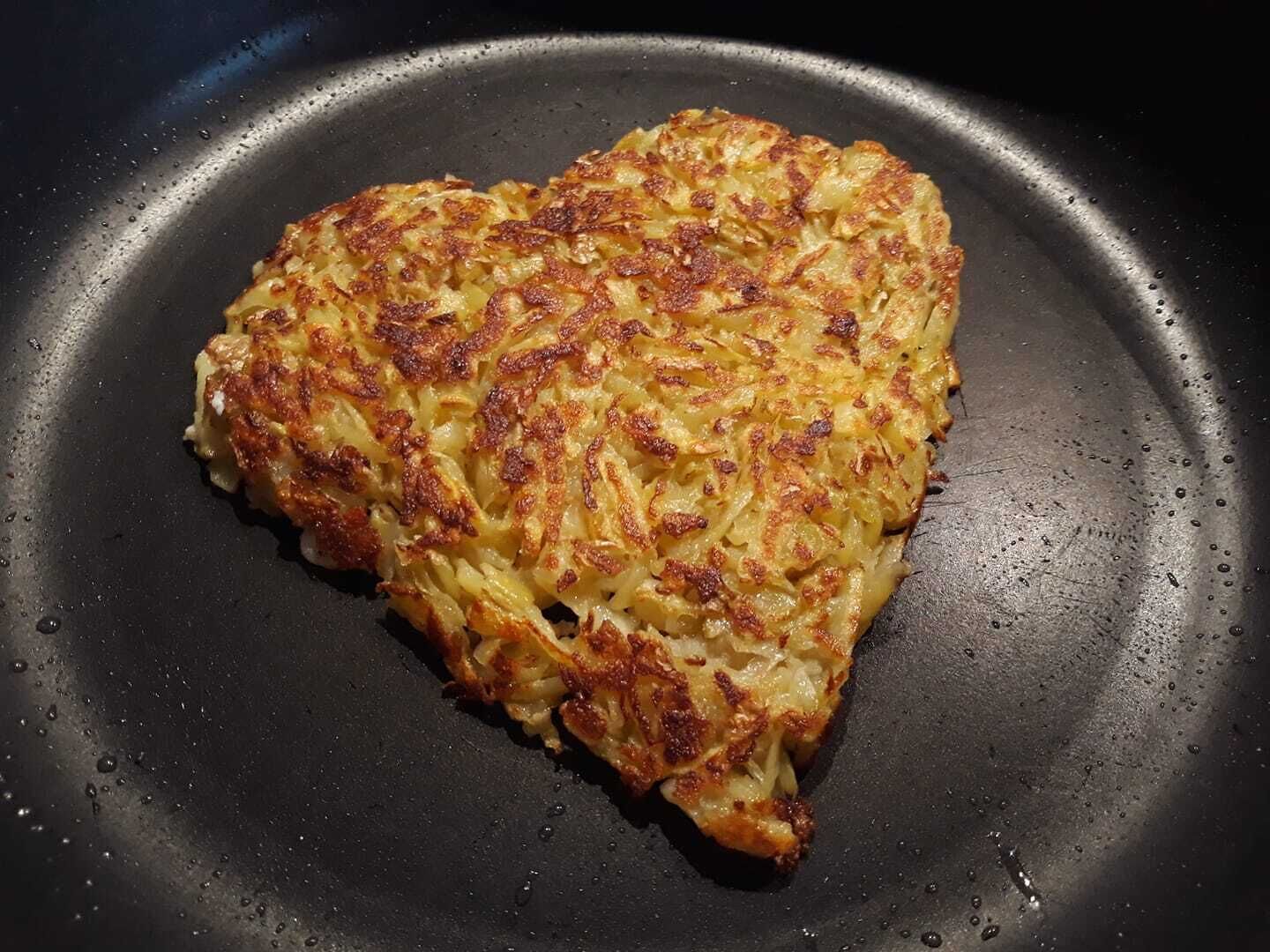 En potatispannkaka formad som ett hjärta, på en stekpanna.