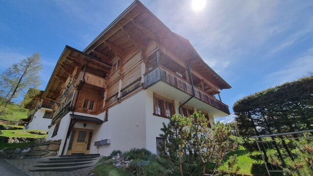 A traditional chalet with a wooden facade, a balcony, and a stone staircase leading to the entrance. - Room with extra-large double-bed, cable TV, private bathroom, organic breakfast, (Lauenen)