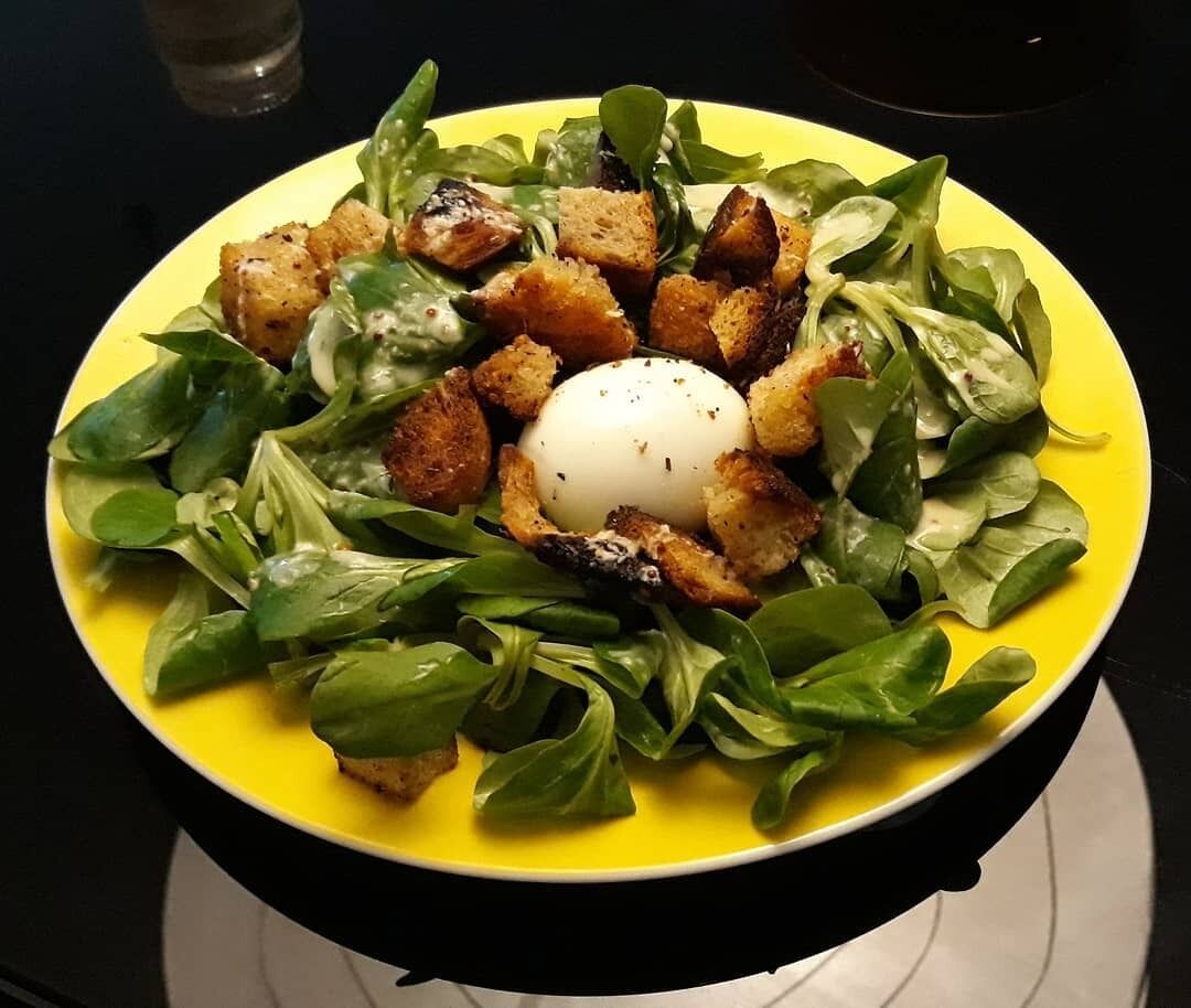 A plate of food with a poached egg, croutons, and greens.