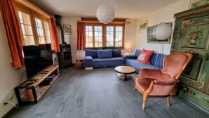 A living room with a sofa, armchair, TV, and a fireplace. - Room with extra-large double-bed, cable TV, private bathroom, organic breakfast, (Lauenen)