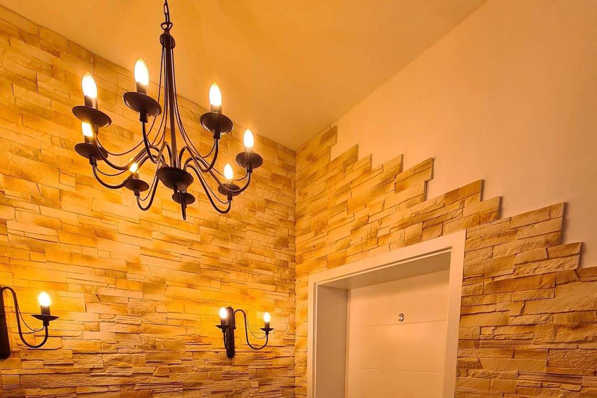 Une pièce avec un mur en pierre, un lustre et une porte.