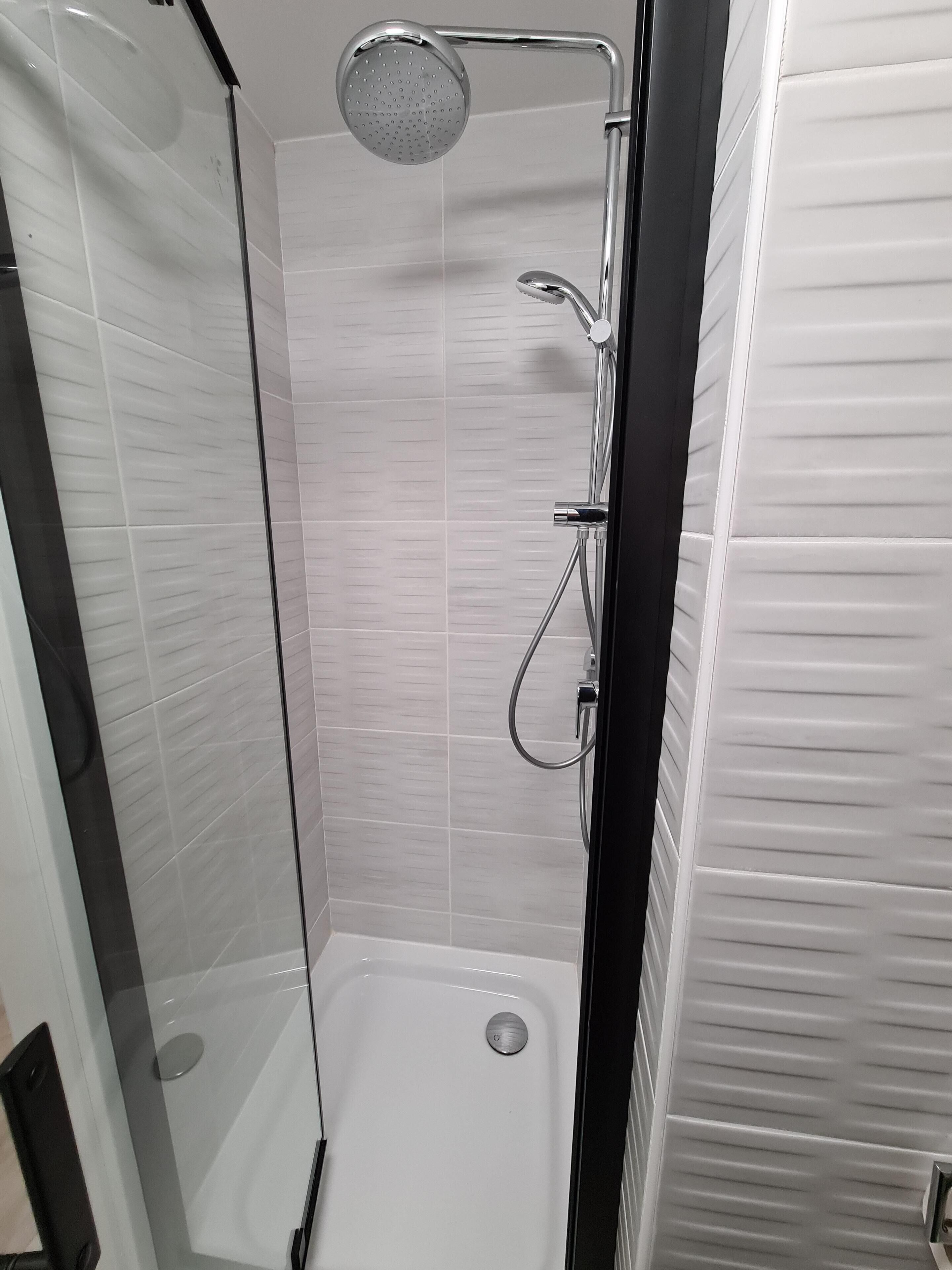 Eine moderne Dusche mit Handbrause und am Wand montiertem Wasserhahn.