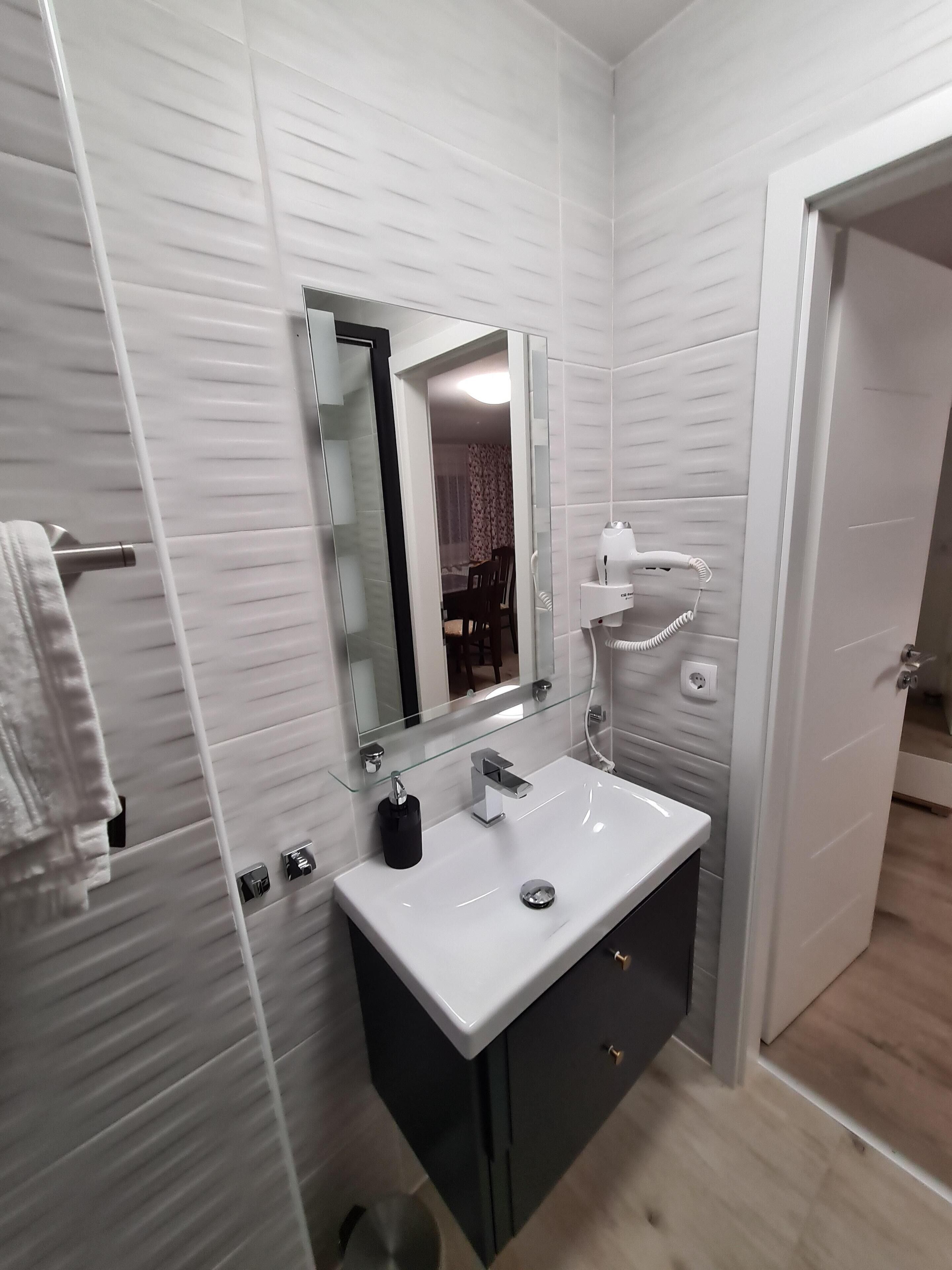 A modern bathroom with a white sink, a mirror, and a shower area.