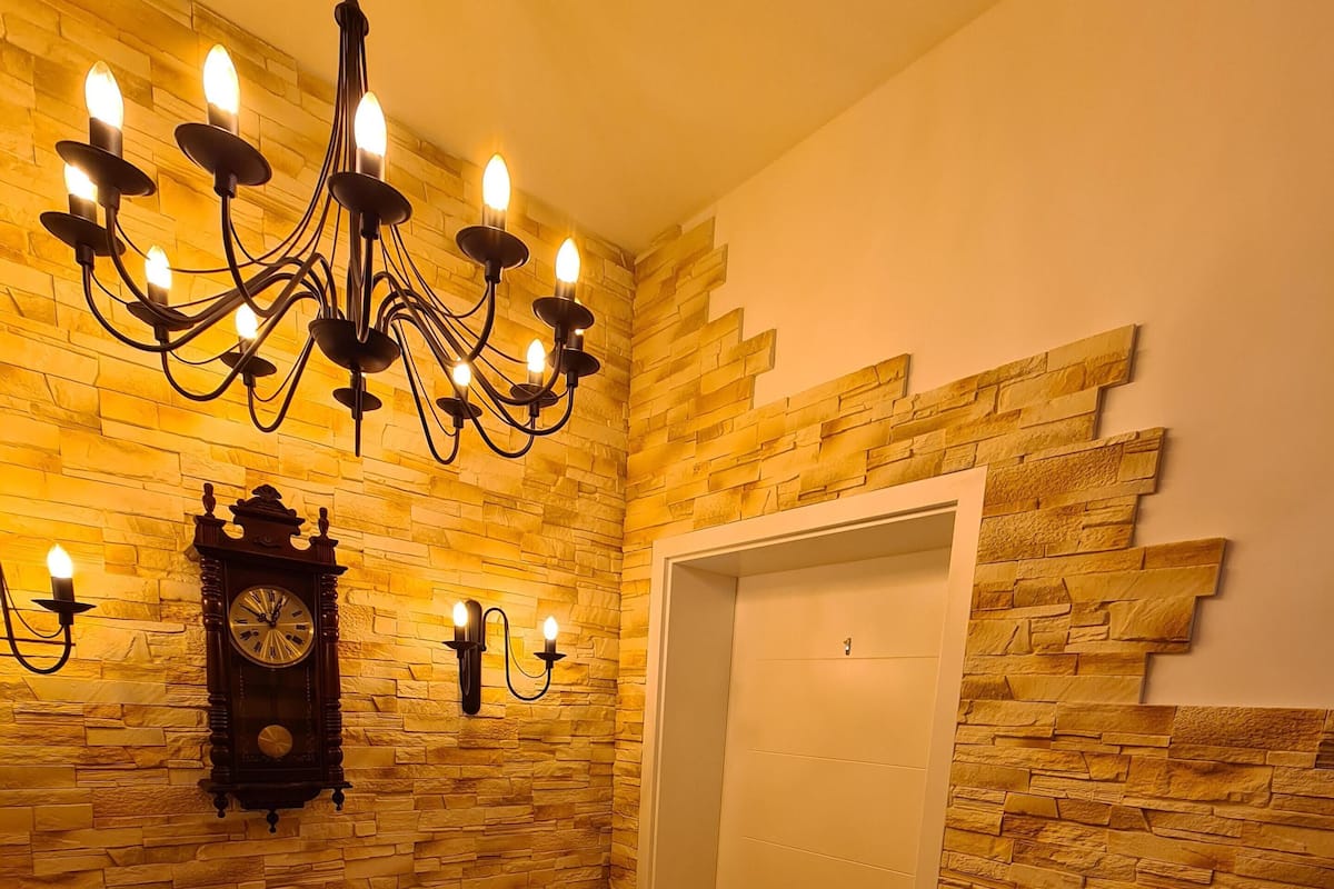 Un escalier avec un mur en pierre, un lustre, des appliques murales, une horloge et une porte.