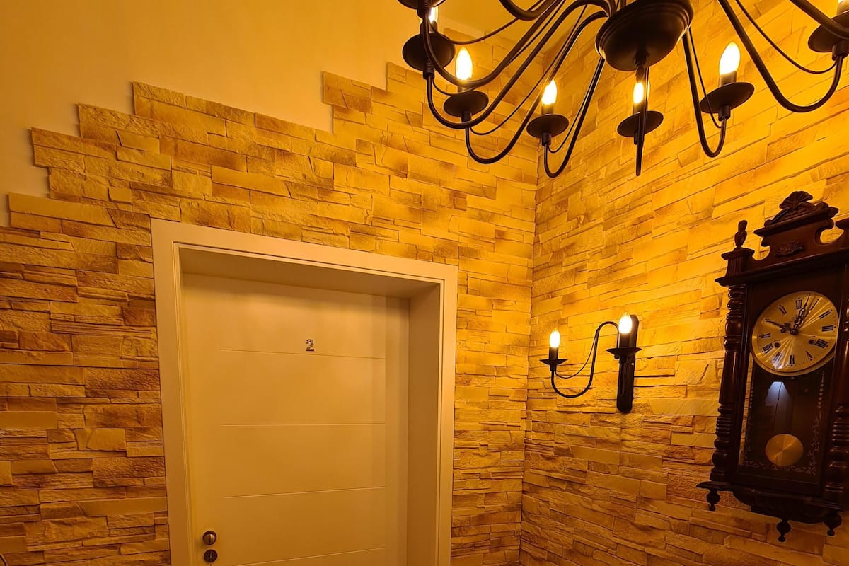 Une pièce avec un mur en pierre, une porte blanche, un lustre, une horloge murale et un chandelier.