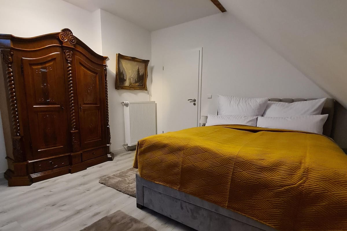 Une chambre à coucher avec un lit, une armoire en bois, un radiateur et un tableau accroché au mur.