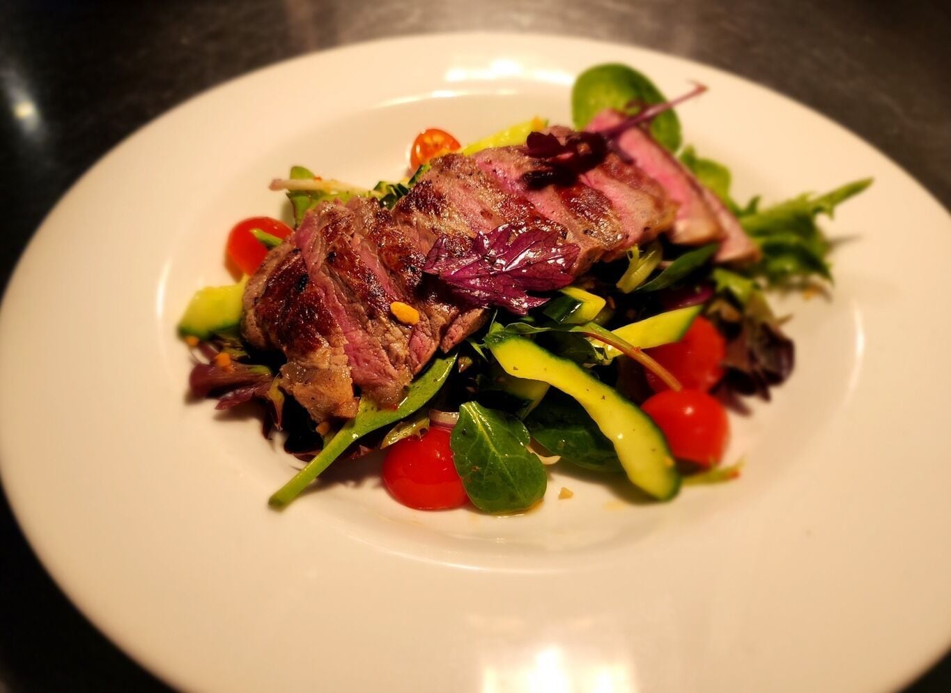 A plate with a grilled steak and a mixed green salad.