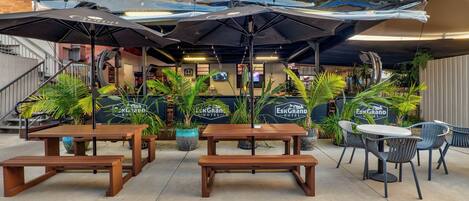 An outdoor seating area with wooden tables and benches, umbrellas, and potted plants at the Esk Grand Hotel.