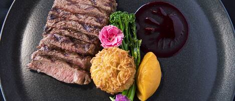 A plate with sliced steak, a dollop of sauce, a piece of fried food, and some greens and flowers.
