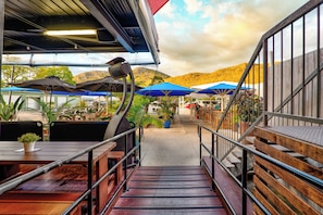 A restaurant with outdoor seating, a staircase leading to a deck, and a view of hills in the background. - Esk Grand Hotel (Esk)