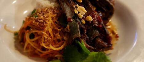 A plate of food with noodles, meat, and peanuts.