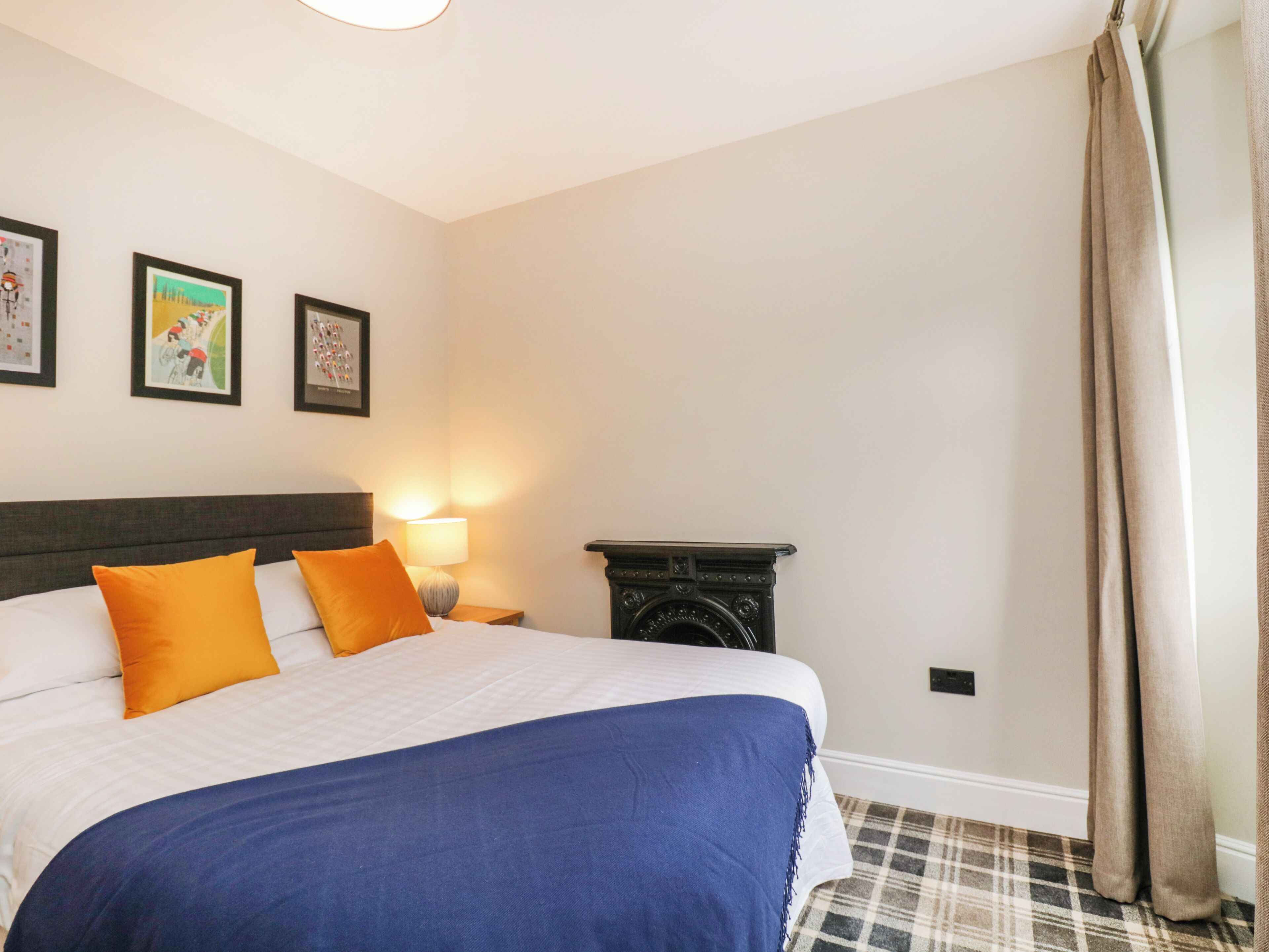 A hotel room with a bed, a nightstand with a lamp, a fireplace, and three framed pictures on the wall.