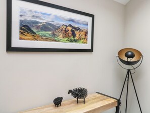 Un cuadro de paisaje enmarco, una lámpara de metal y dos esculturas de ovejas de metal sobre un estante de madera.
