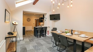 Una cocina moderna con comedor, que incluye una mesa de madera, taburetes de bar y un televisor montado en la pared.