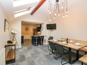 A modern kitchen with a dining area, featuring a wooden table, bar stools, and a TV mounted on the wall. - Netherbeck (Ambleside)
