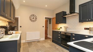 Una cocina moderna con armarios oscuros, encimera blanca, horno empotrado y un reloj de pared.