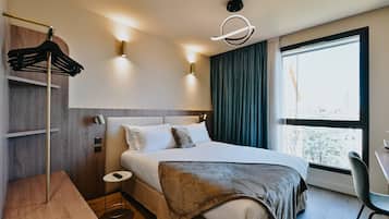 Una habitación de hotel moderna con una cama grande, una mesita de noche, una silla, un perchero y una ventana con vistas.