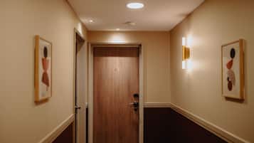 A hallway with a wooden door labeled "42", light fixtures on the walls, and framed artwork on either side.