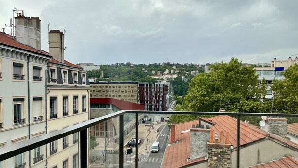 Vista desde un balcón con vistas a un paisaje urbano que incluye edificios, una calle y una colina al fondo.