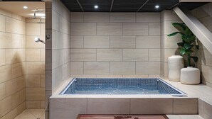 Un baño moderno con una bañera grande, zona de ducha y escalones de madera que dan a un espacio de descanso.