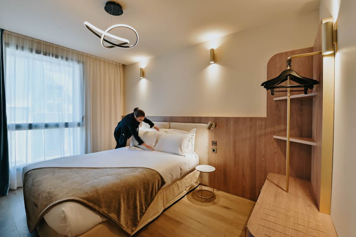 A modern hotel room with a large bed, bedside tables, a wardrobe, and a hanging coat rack.