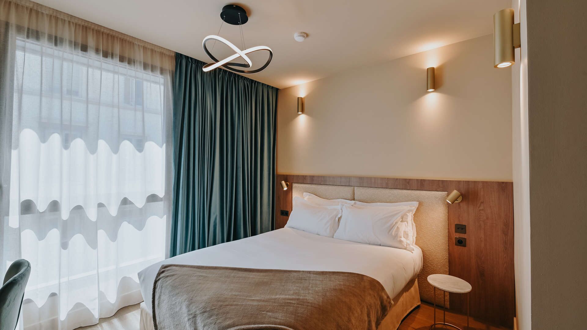 A hotel room with a large bed, a modern chandelier, and a view of the city through the window.