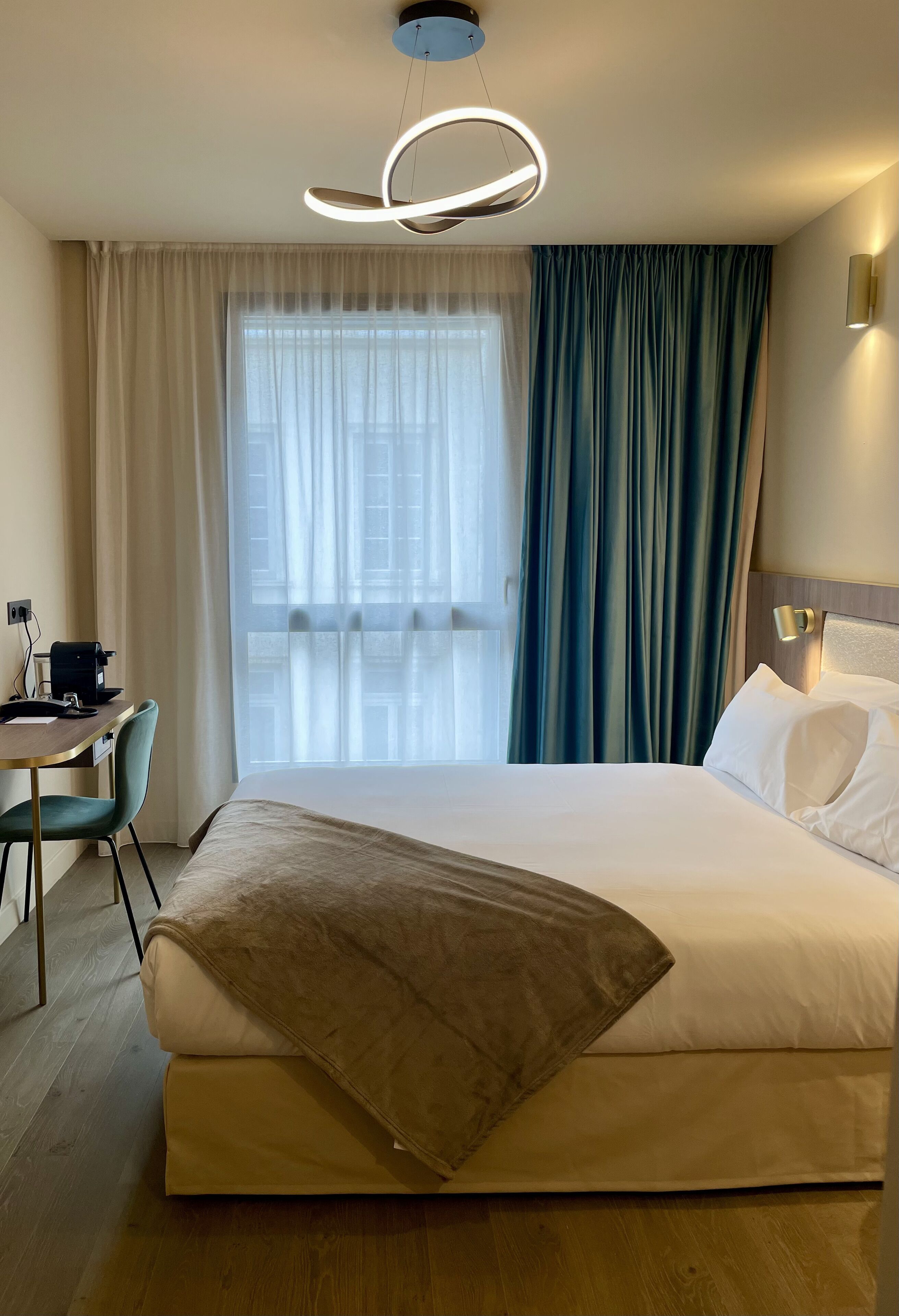 Une chambre d’hôtel avec un grand lit, un bureau avec une chaise, une machine à café et une fenêtre avec des rideaux.